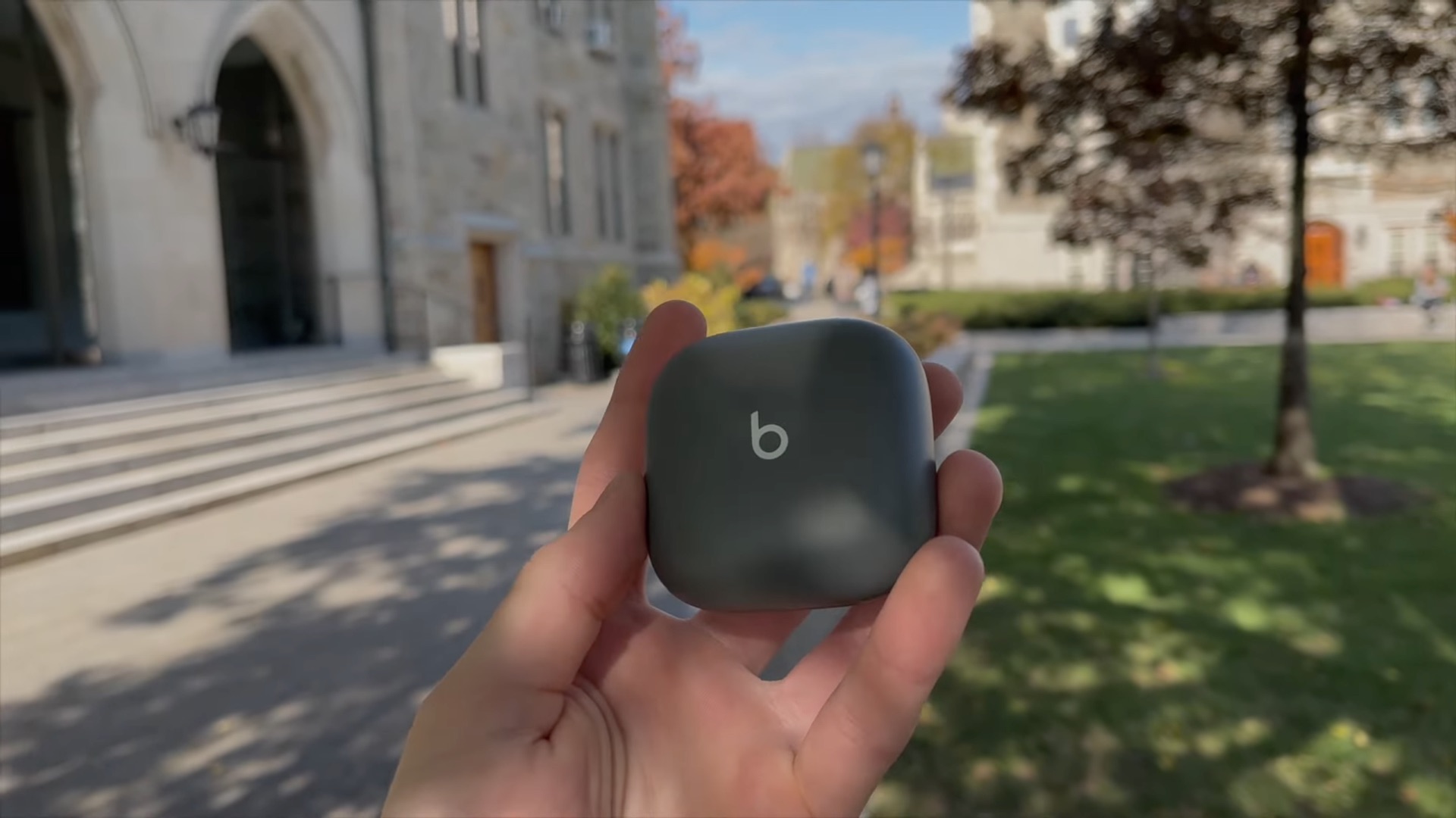 La main d'un jeune homme tenant un étui de chargement sans fil fermé pour les écouteurs Beats Fit Pro dans un parc universitaire
