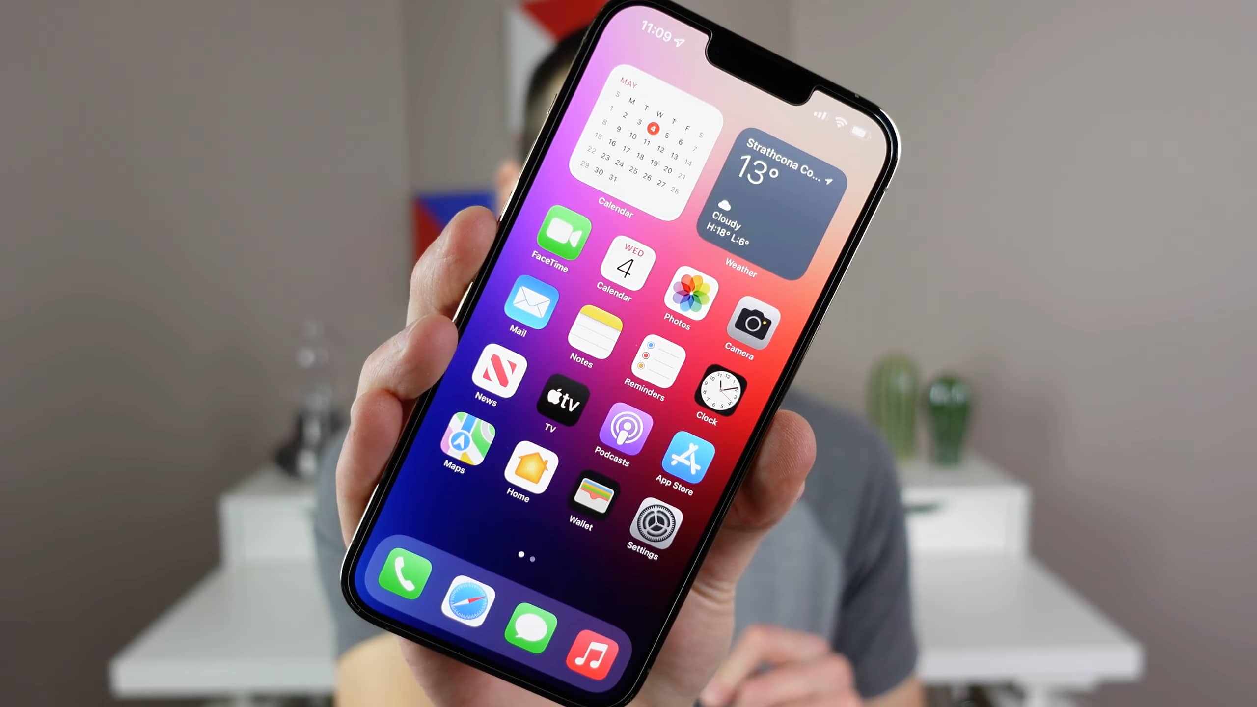 Apple's iPhone 13 Pro Max with home screen widgets and app icons is being held in front of the camera in this still image screenshotted from iDownloadBlog's video walkthrough covering 15 iPhone settings designed for optimal experience