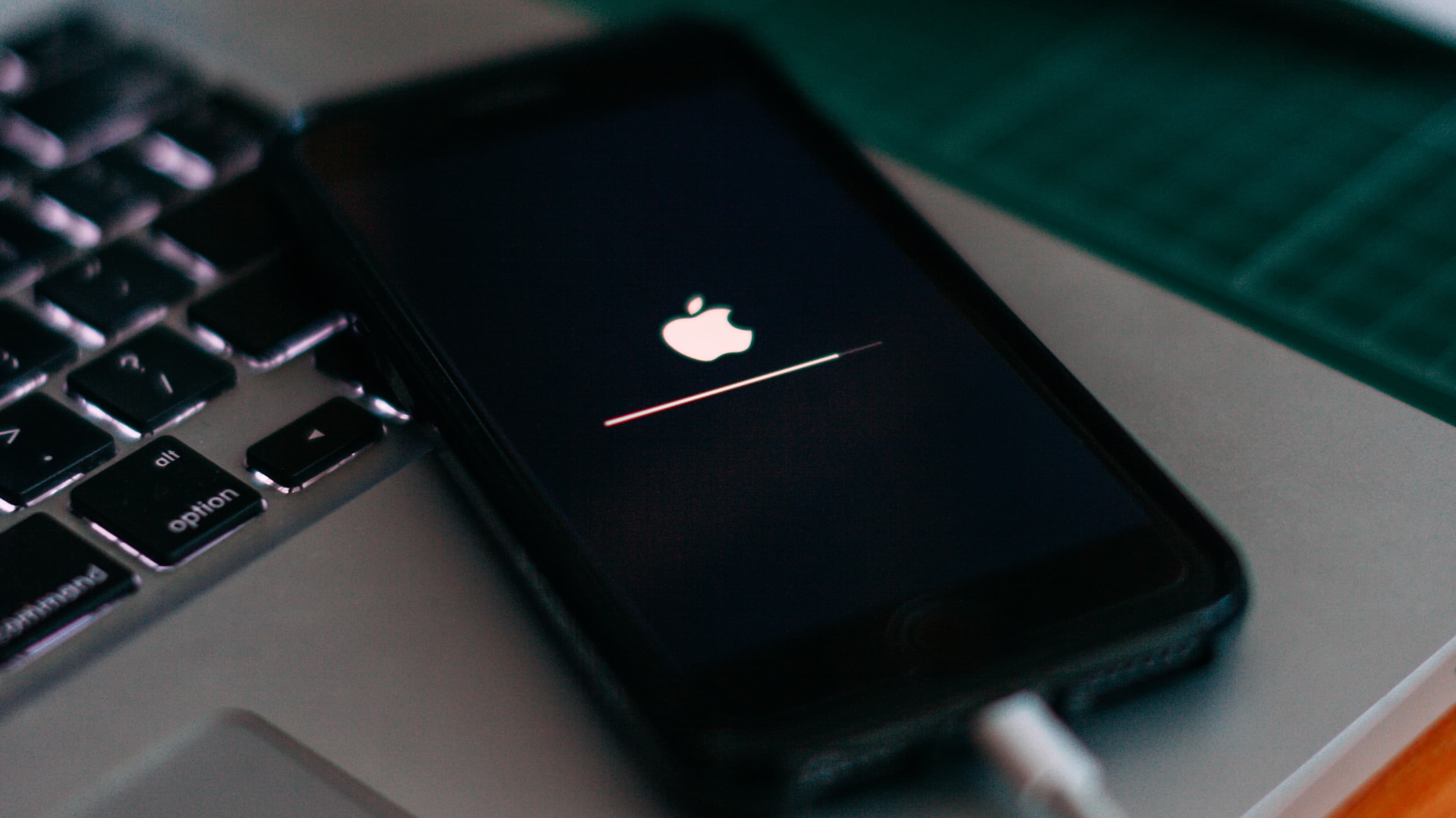 Un iPhone posé sur un MacBook, affichant une barre de progression de la mise à jour iOS