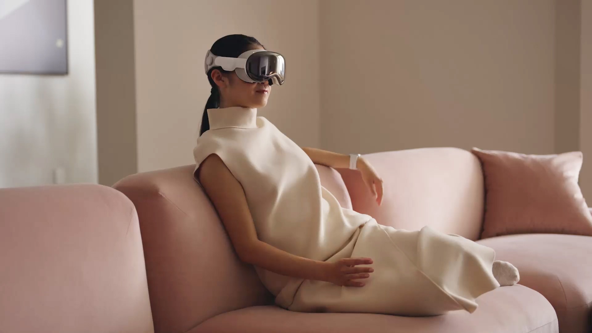 Woman sitting on a couch, wearing Apple's Vision Pro headset and performing hand gestures